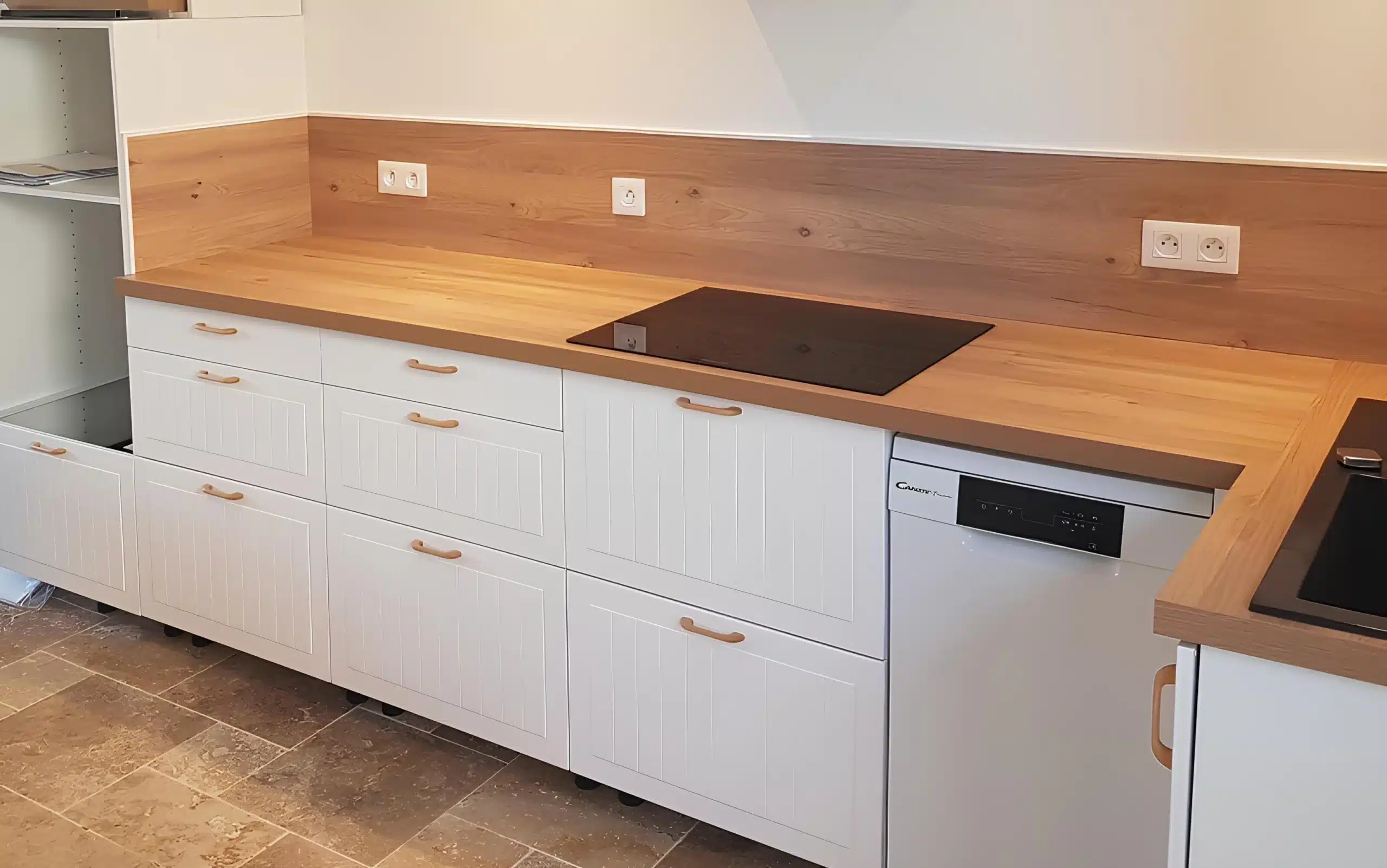 Cuisine neuve avec meubles blancs rainurés, plan de travail et crédence en bois clair, plaque de cuisson noire et lave-vaisselle Candy intégrés.