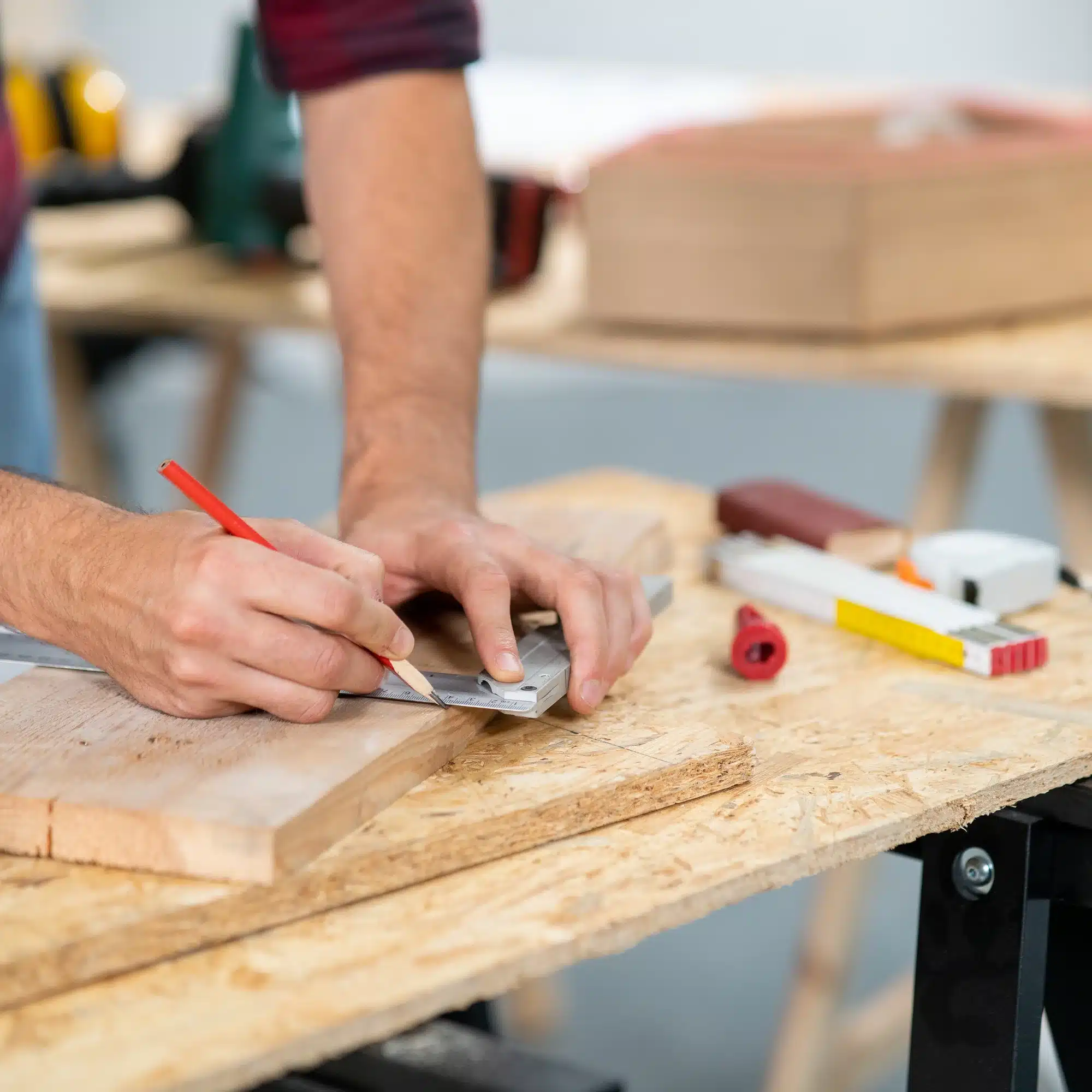 Ébéniste en action : Traçage de précision pour la menuiserie. Gros plan : ébéniste en tablier traçant des marques précises sur du bois brut à l'aide d'un crayon et d'une équerre. Maillet et copeaux sur l'établi.