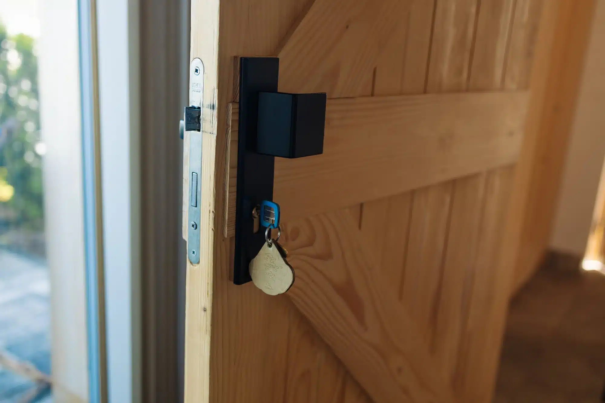 Poignée noire carrée moderne sur porte bois clair ouverte. Une clé et son porte-clés sont dans la serrure ASSA ABLOY visible.