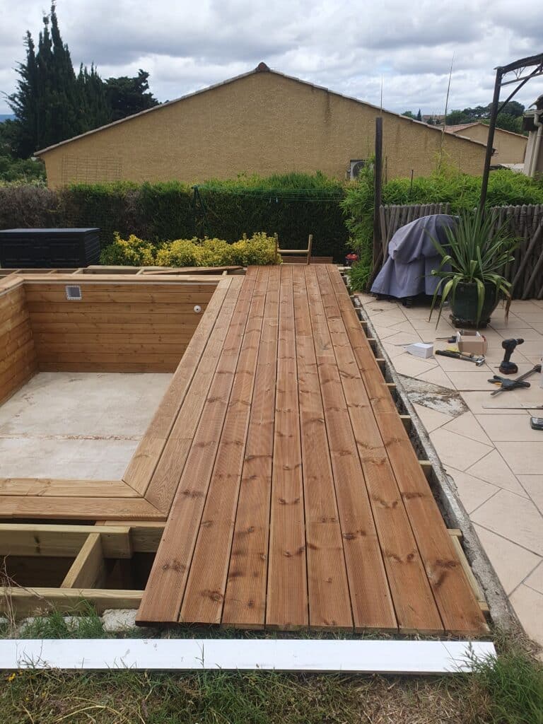 Construction Terrasse Bois et Aménagement Piscine Jardin Pose d'une terrasse en bois rainuré bordant une piscine en construction dans un jardin.